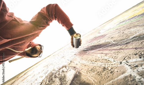 Lower view of street artist painting graffiti on generic wall - Modern art concept with urban guy performing and preparing live murales with green aerosol color spray - Warm retro backlight filter