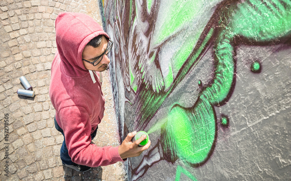 Fototapeta premium Uliczny artysta malujący kolorowe graffiti na ścianie rodzajowej - koncepcja sztuki współczesnej z miejskim facetem wykonującym i przygotowującym żywe muraly z zielonym aerozolowym sprayem - neutralny filtr słoneczny popołudnie