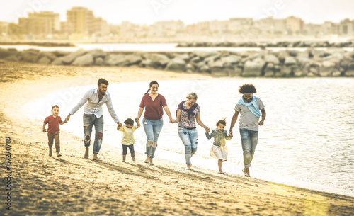 Happy multiracial families running together at beach holding hands on vacation - Multicultural summer joy concept with mixed race people having fun outdoor at sunset - Warm vintage backlight filter