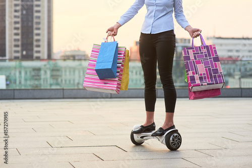 Woman holding colorful bags. Person riding gyroscooter. Ultimate shopping guide.