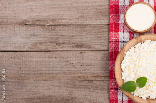 Cottage cheese in a wooden bowl with sour cream on old wooden background with copy space for your text. Top view