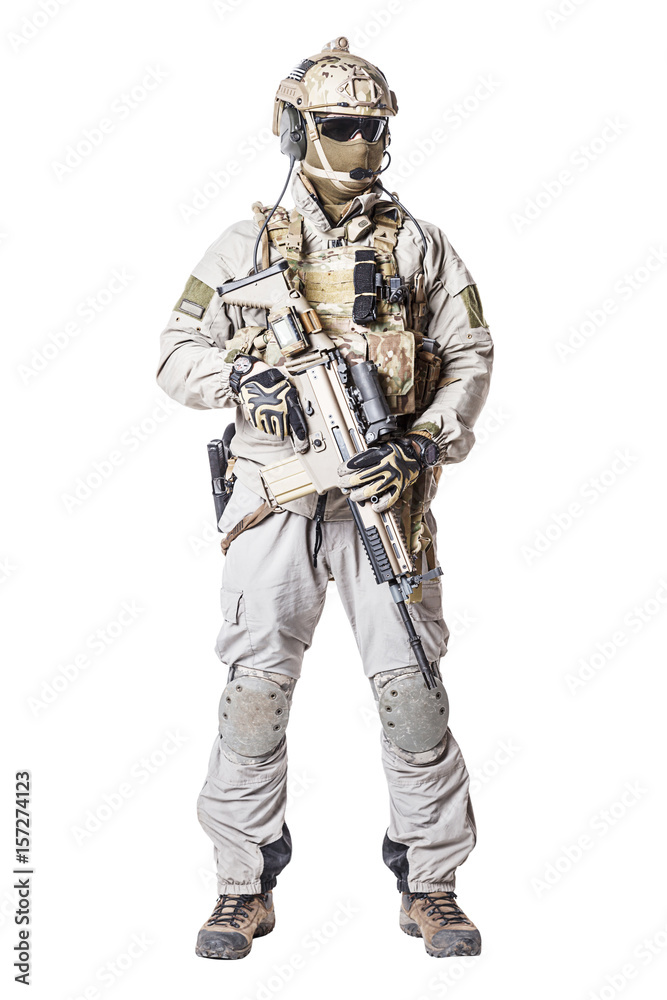 Army soldier in Protective Combat Uniform holding Special Operations Forces Combat Assault Rifle. Knee pads, mag recovery pouch, chest rig, military boots. Studio shot, isolated on white