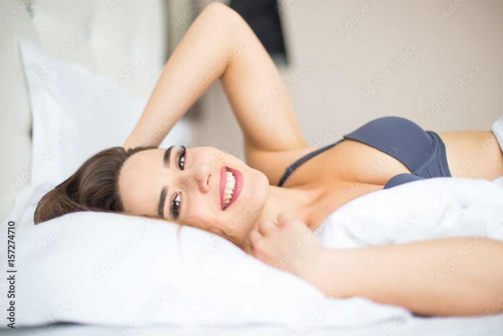 Young woman looking at camera and smiling while lying on the bed at home