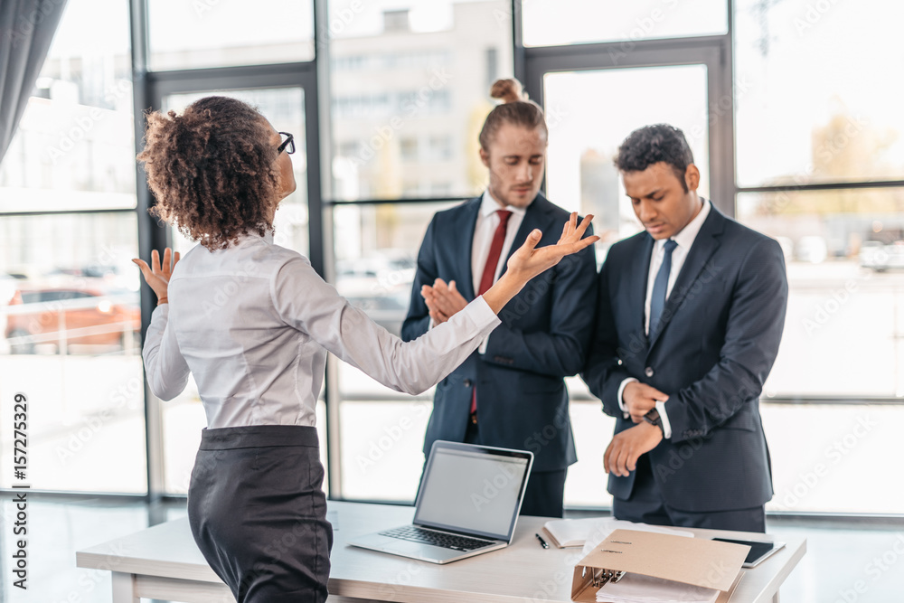 Young businesswoman gesturing and arguing with coworkers in office, business team meeting concept Young businesswoman gesturing and arguing with coworkers in office, business team meeting concept