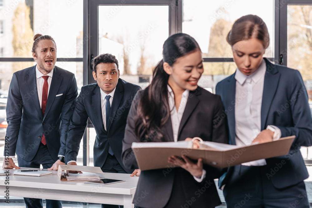 Young businesswomen working together while businessmen grimacing behind, business team working concept Young businesswomen working together while businessmen grimacing behind, business team working concept