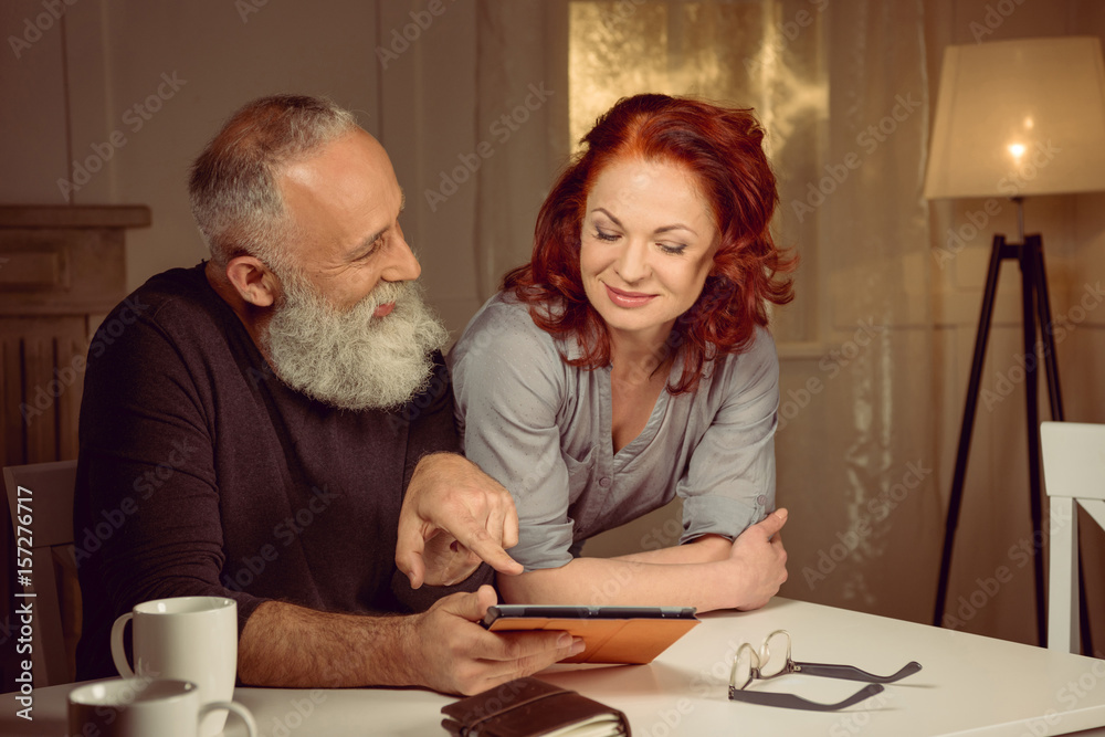 middle aged couple using digital tablet while sitting at table at home middle aged couple using digital tablet while sitting at table at home