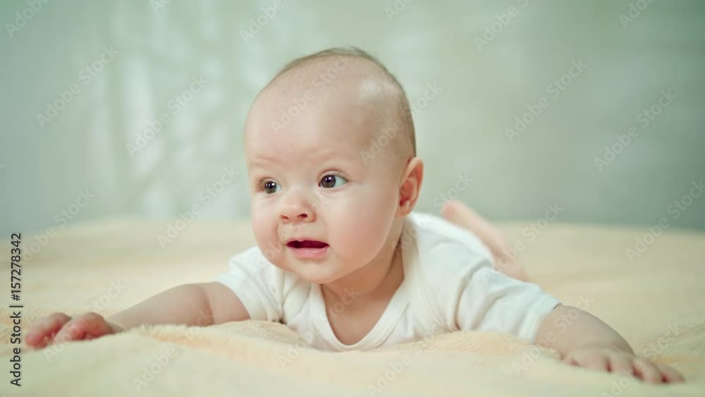 Baby lying on stomach on a soft orange linen in bed and playing. Close-up shot, soft focus Baby lying on stomach on a soft orange linen in bed and playing. Close-up shot, soft focus