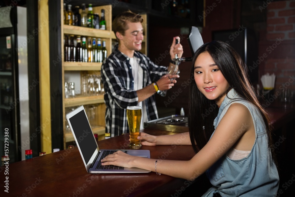 Woman having beer while using laptop at bar counter