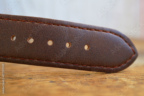  Macro detail of a brown leather wrist watch strap on the wooden background 