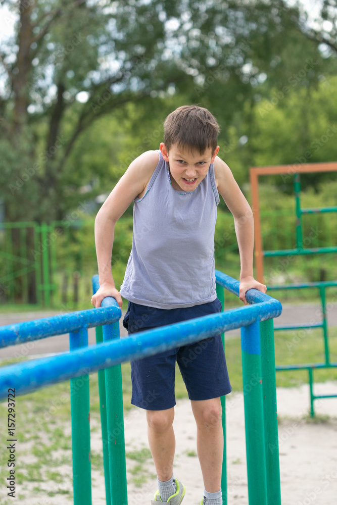 The teenager in a vest is engaged on uneven bars The teenager in a vest is engaged on uneven bars