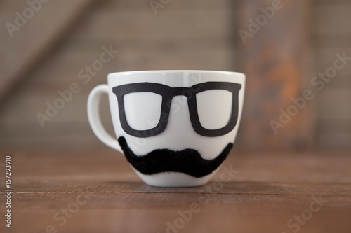 Coffee cup with mustache and eyeglasses on table