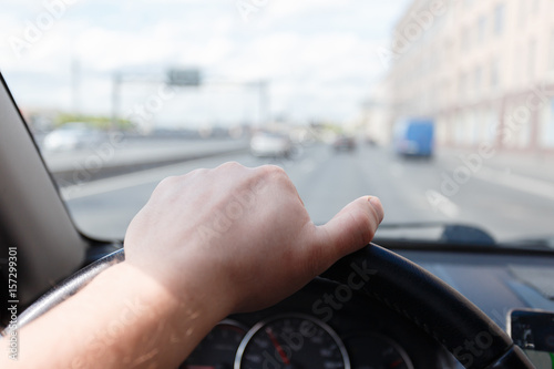 Male hand on the steering wheel while the car is in motion in city.
