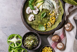 Green spinach matcha tortilla with vegan ingredients for filling. Sweet corn, avocado, green paprika, sprouts, mushrooms served in terracotta plate over gray texture background and textile. Flat lay