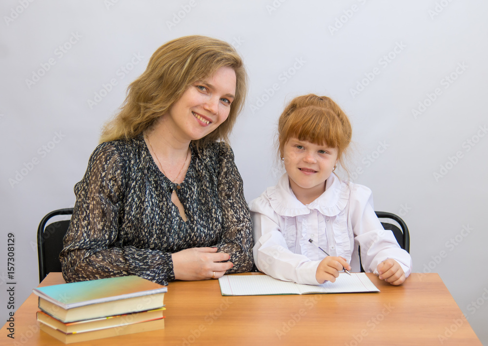 Little girl with her mother writes at the table with exercise books and textbooks Little girl with her mother writes at the table with exercise books and textbooks