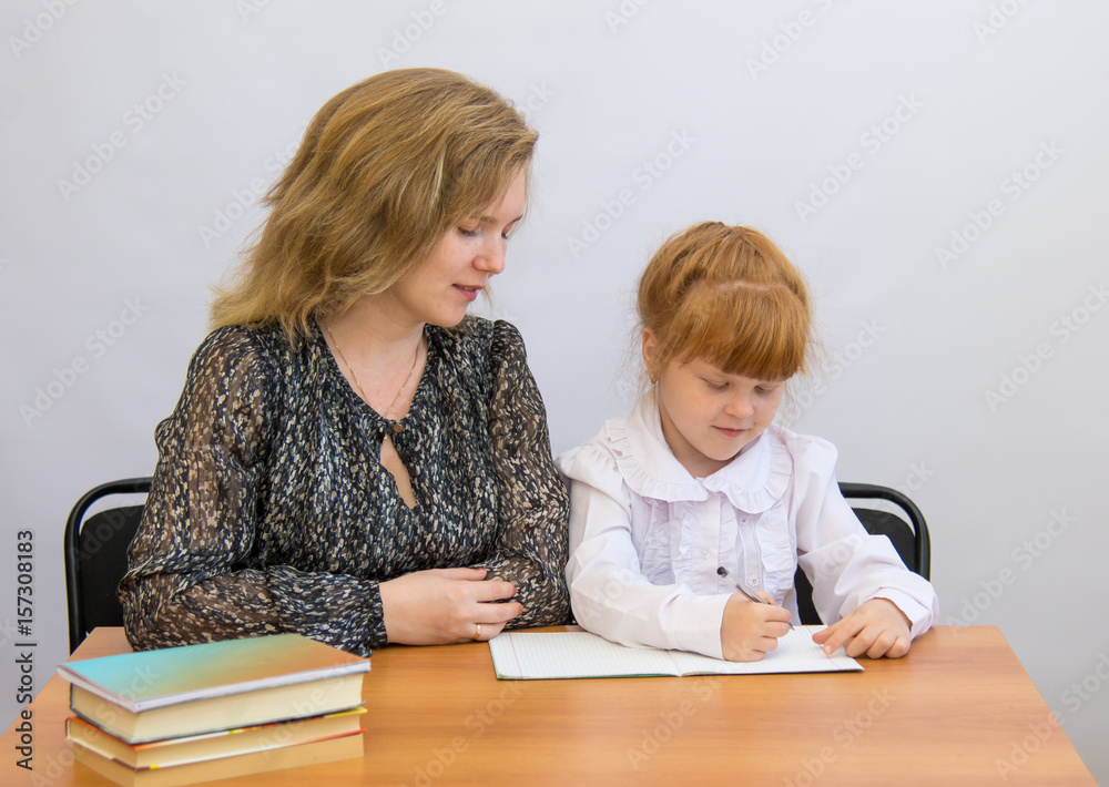 Little girl with her mother writes at the table with exercise books and textbooks