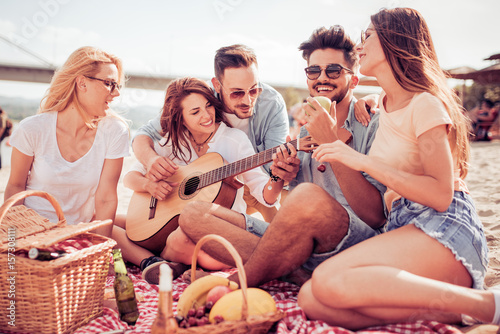 Happy young friends relaxing and playing guitar at the beach