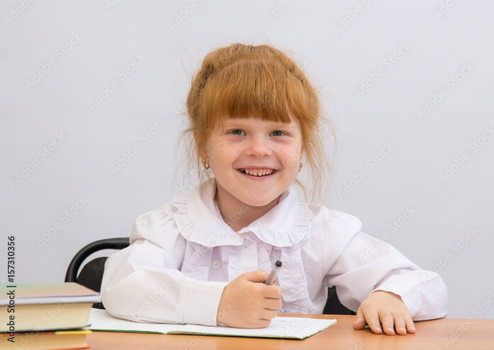 Little girl at the desk cheerfully laughs Little girl at the desk cheerfully laughs