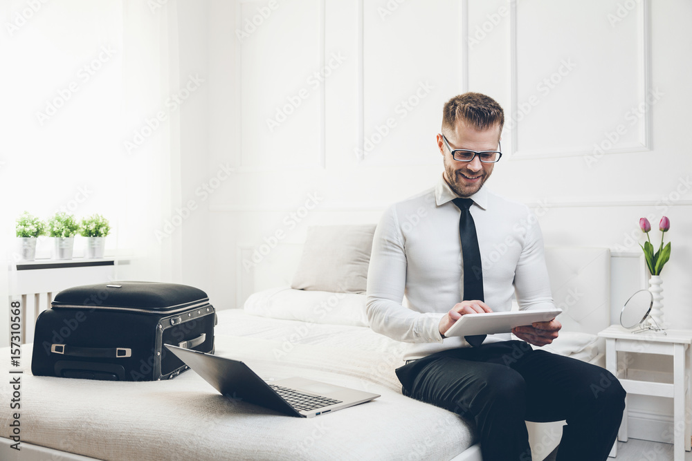Businessman on bed working with a tablet and laptop from his hotel room Businessman on bed working with a tablet and laptop from his hotel room