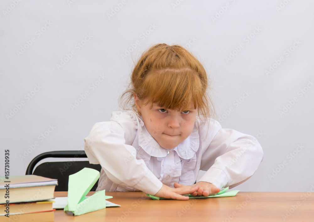 The little girl at the table carefully smooths the paper at the fold The little girl at the table carefully smooths the paper at the fold