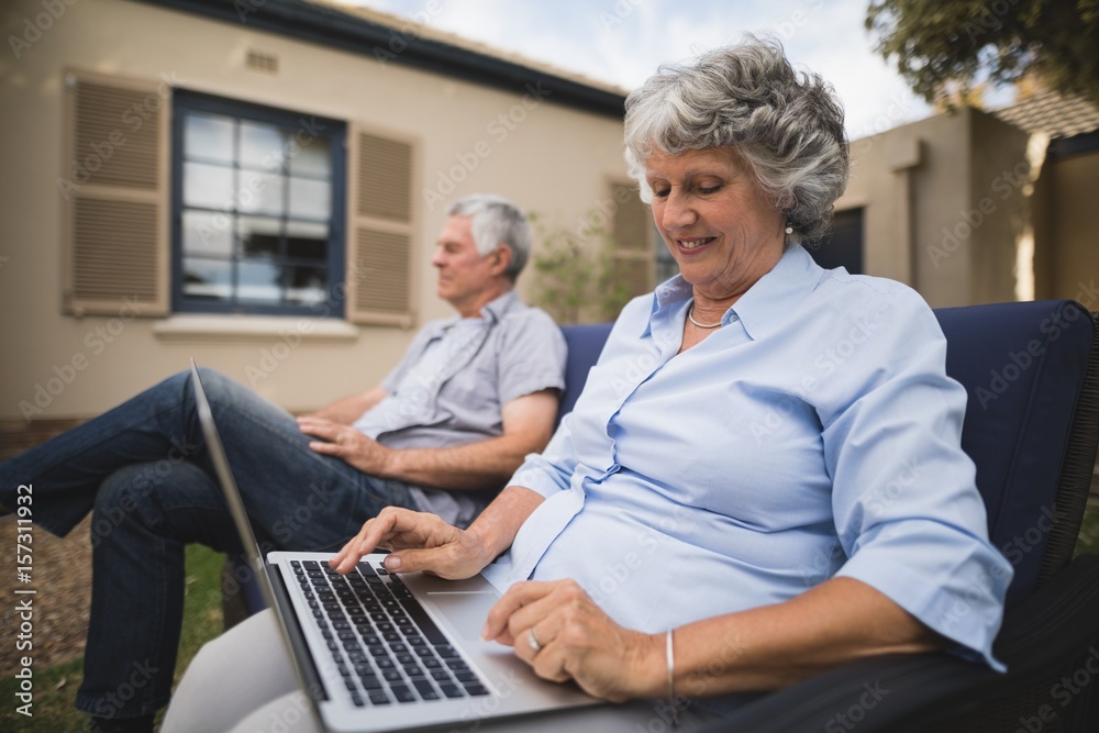 Senior woman using laptop while sitting on couch in backyard Senior woman using laptop while sitting on couch in backyard