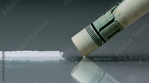 Drug Abuse. A rolled banknote snorting a line of cocaine powder. Problems with drugs concept. Grey background. Close-up macro shot.