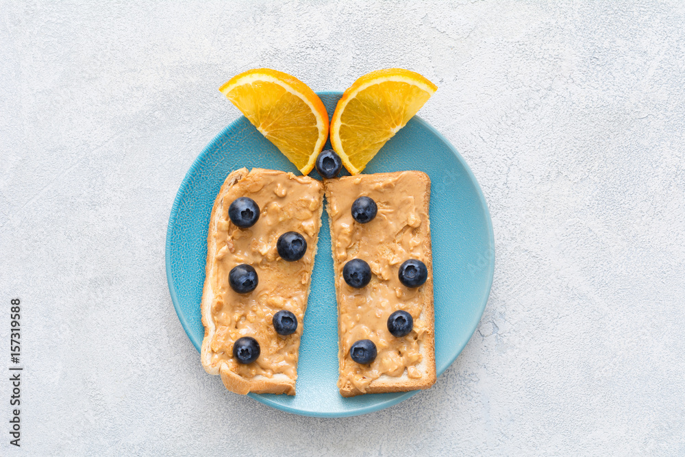 Butterfly shaped peanut butter toast with fresh blueberries on a blue plate. Top view. Healthy breakfast / snack meal for kids