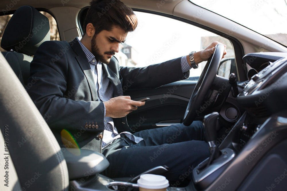 Handsome businessman texting message on the phone while driving  car unsecured without fastening seat belt.Safety concept.