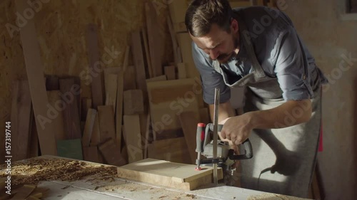 20s bearded woodworker works with brashing machine at sunny day in workshop photo