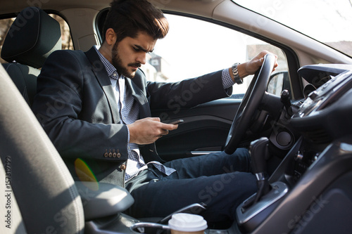 Handsome businessman texting message on the phone while driving car unsecured without fastening seat belt.Safety concept.