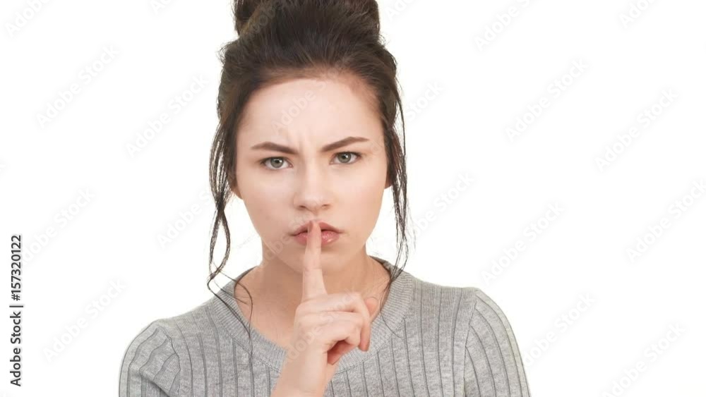 Strict young teenager girl with brunette hair putting her finger to lips and calling to silence. Footage on white background in slowmotion Strict young teenager girl with brunette hair putting her finger to lips and calling to silence. Footage on white background in slowmotion