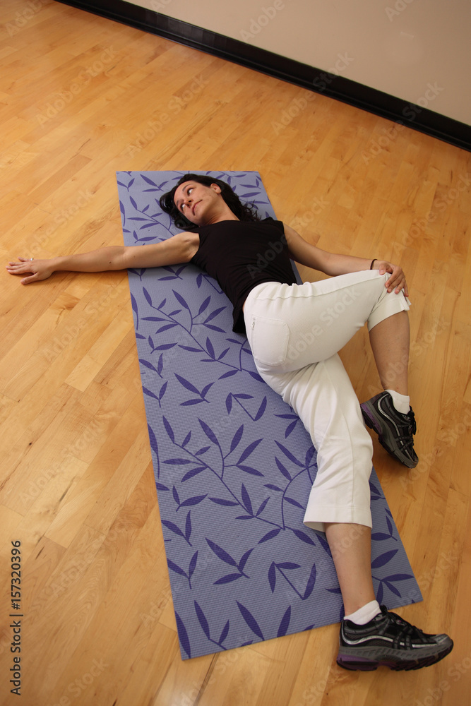 Young fit woman crosses knee over leg and stretches at gym