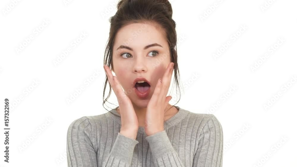 Very surprised Caucasian teenager girl with brunette hair covering mouth with hand and looking astonished on white background in slowmotion Very surprised Caucasian teenager girl with brunette hair covering mouth with hand and looking astonished on white background in slowmotion