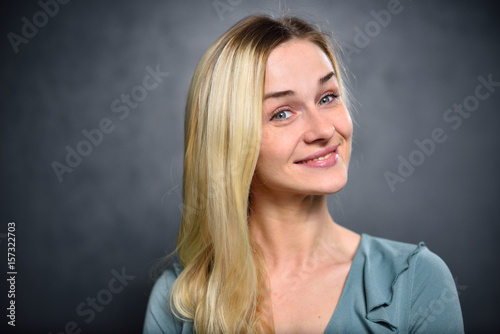Blonde girl with a cunning smile on a gray wall background