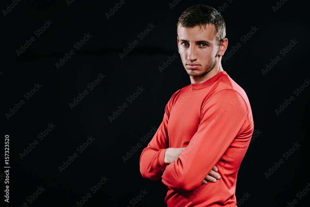 Athlete man in red sportswear standing over dark background, holding hands on his waist. Lifestyle, sport, motivation.