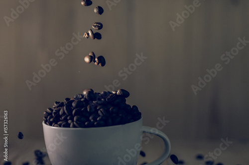coffee beans is drop on cup with wooden background, effect filter and low key lighting.