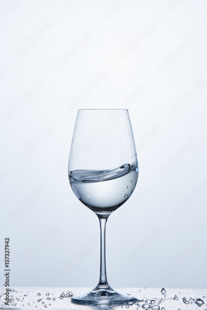 Pure water wave in the wine glass while standing on the glass with water bubbles against light background. Pure water wave in the wine glass while standing on the glass with water bubbles against light background.