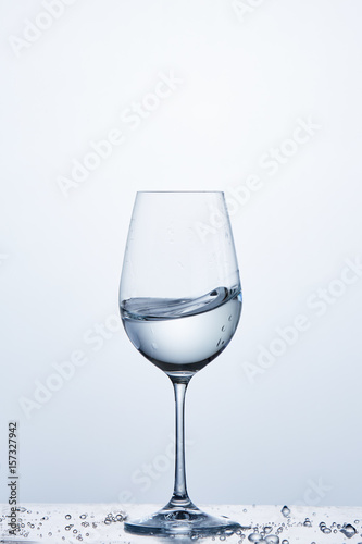Pure water wave in the wine glass while standing on the glass with water bubbles against light background.