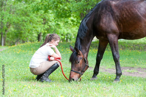 Young teenage girl owner sitting close to her favorite horse
