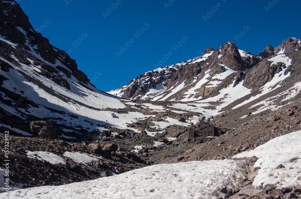 Obraz premium Toubkal national park in springtime with mount, cover by snow and ice, Refuge Toubkal, start point for hike to Jebel Toubkal, – highest peak of Atlas mountains and Morocco