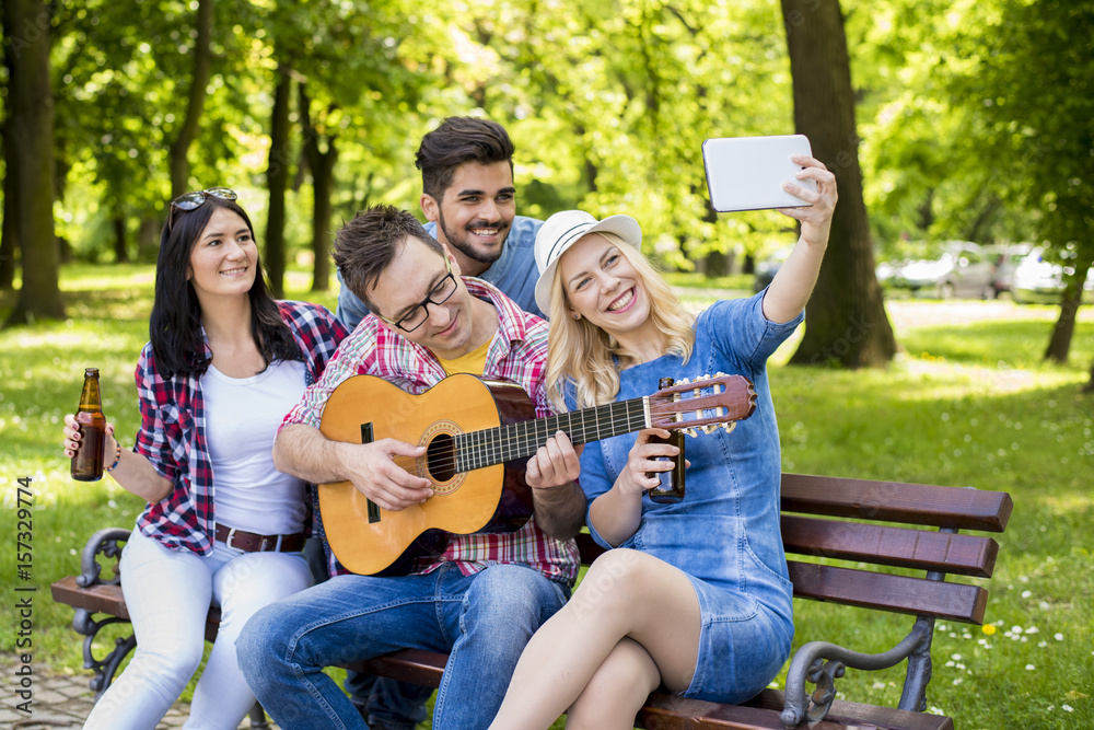 Group of friends having fun in the park while playing guitar and taking selfie