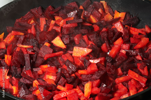 Cut-up red beet and carrot are frying in pan