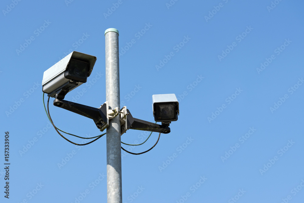 Two cctv surveillance cameras on a high street pylon against the clear blue sky, concept for safety and security against vandalism, crime or terrorism Two cctv surveillance cameras on a high street pylon against the clear blue sky, concept for safety and security against vandalism, crime or terrorism