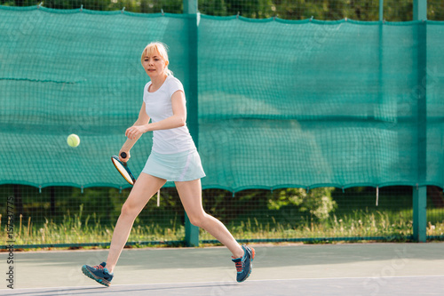 Tennis player playing on the court on a sunny day. Young sport woman training outdoors. Healthy lifestyle concept.
