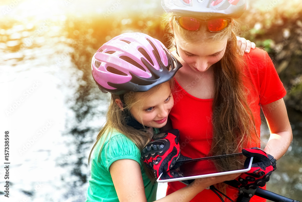 Obraz premium Bikes cycling girl. Children rides bicycle. Bicyclist girl watch on tablet computer. Kids looking for way. Dependence of adolescents on gadgets. Sports orienteering.