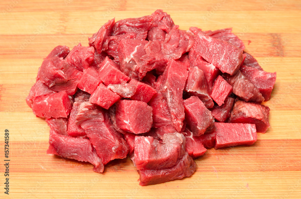 Portion of red meat sliced into cubes over a wooden board