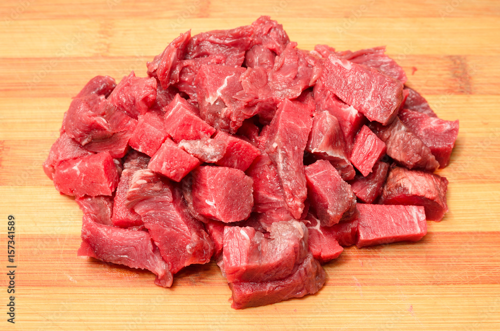 Portion of red meat sliced into cubes over a wooden board Portion of red meat sliced into cubes over a wooden board