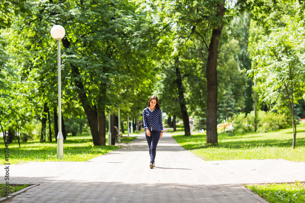 Fototapeta premium Beautiful young woman walking in green summer park