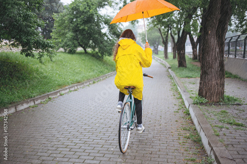 Rear view of bicycle rider wearing raincoat while cycling with umbrella