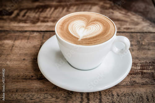 Drak tone filter,Close up white coffee cup with heart shape latte art on wood table at cafe photo