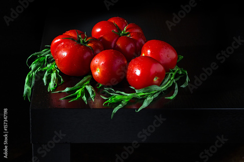 Juicy tomatoes with estragon and water dropletson a wooden dark background photo